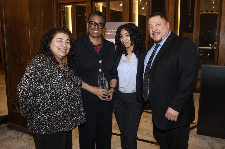 Sharon Johnson Coleman holds a glass award in her hand, surrounded by members of the Parsons family wearing formal attire. They all smile at the camera.