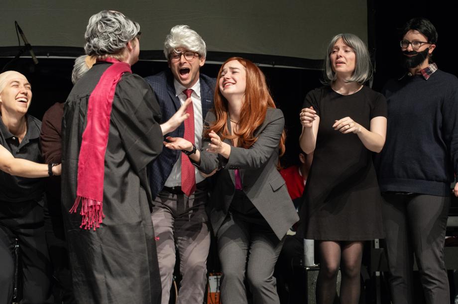 Students in wigs and costumes hold their arms out to the student playing Judge Easterbrook.