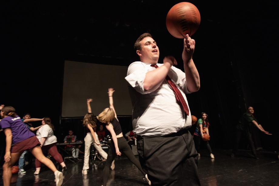 A man in a shirt and tie spins a basketball on his finger.