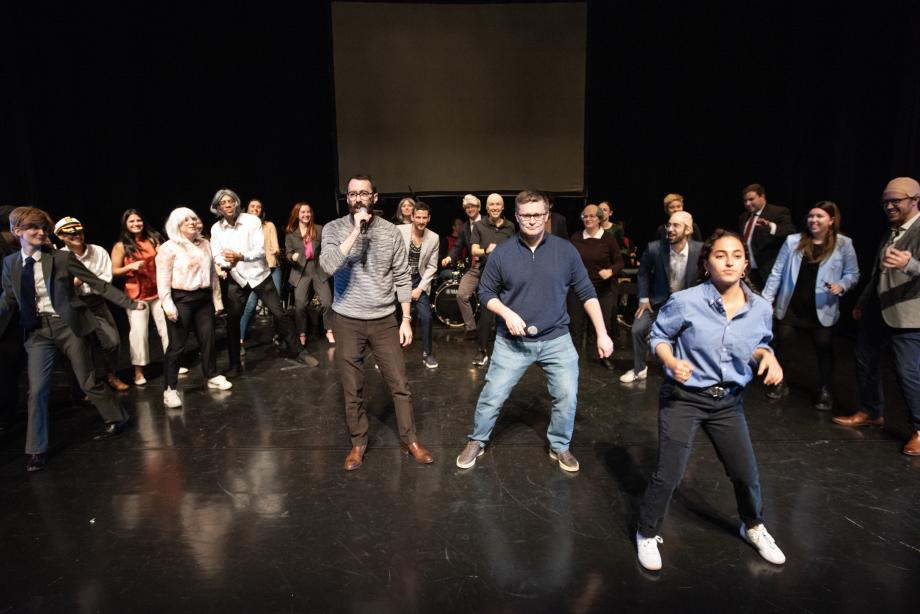 Professors Rappaport and Casey hold microphones in their hands as they move side to side with students dancing with them.