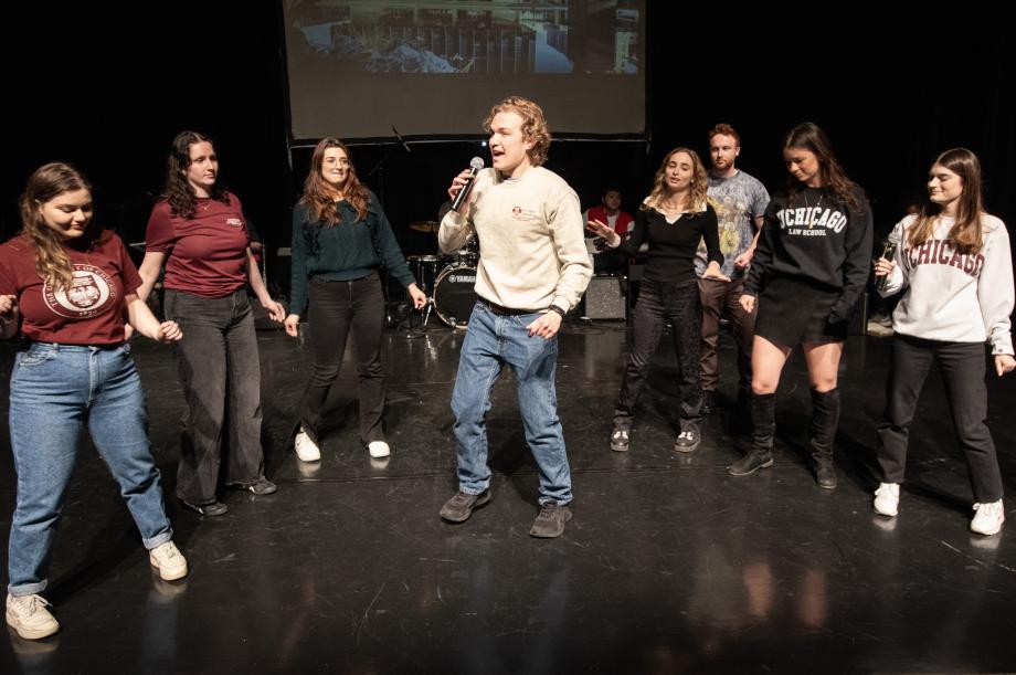 Students create a semi-circle around a man with a microphone in his hand.