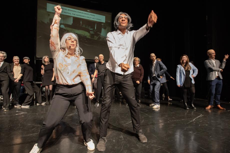 Two students in wigs pump their arms as others look on behind them.