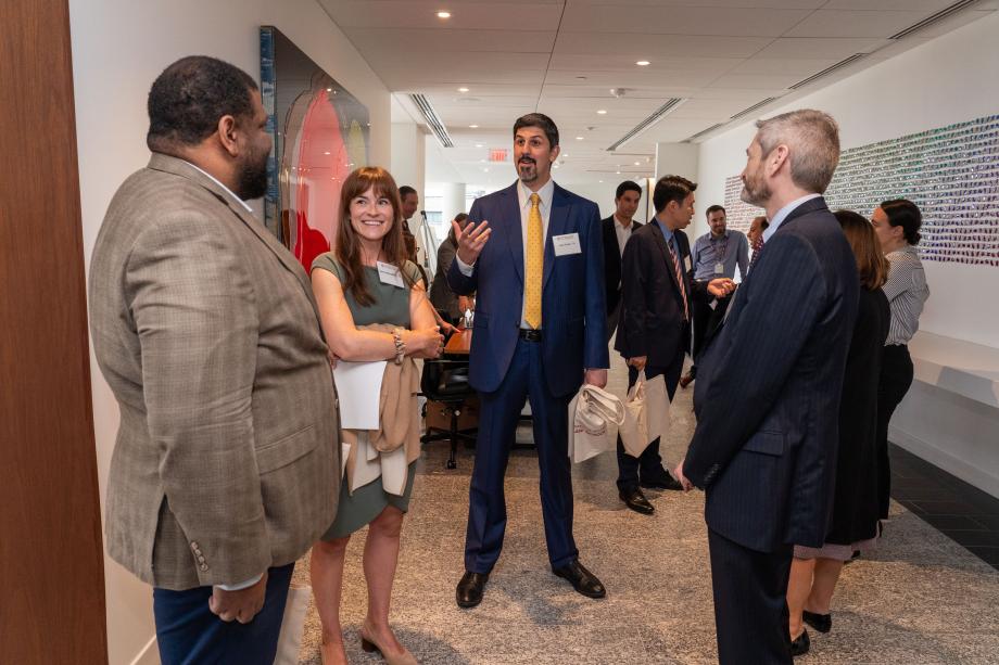 Dean Thomas J. Miles caught up with Rubenstein Scholar graduates. A group of four people stand in a circle, conversing with one another. One, in a blue suit and yellow tie, gestures with his hand while speaking.
