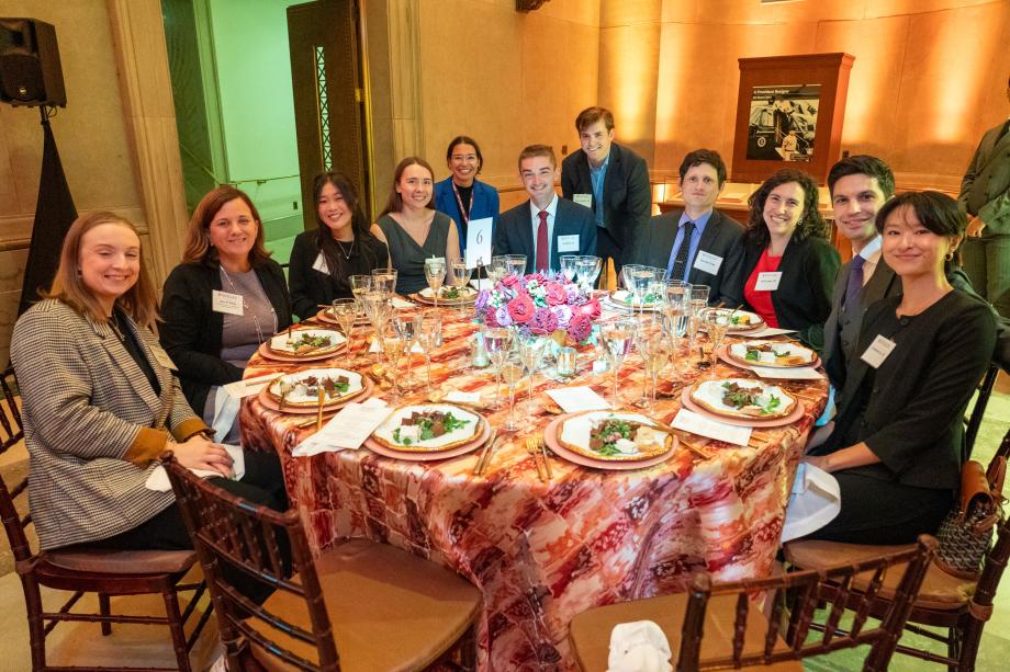 Attendees reminisced and reconnected with one another. Thank you for celebrating 10 years of graduating classes of the David M. Rubenstein Scholars Program! Attendees seated at a large circular table with salad plates in front of each person. The attendees crowd around the further half of the circular table to pose for the picture with smiles.