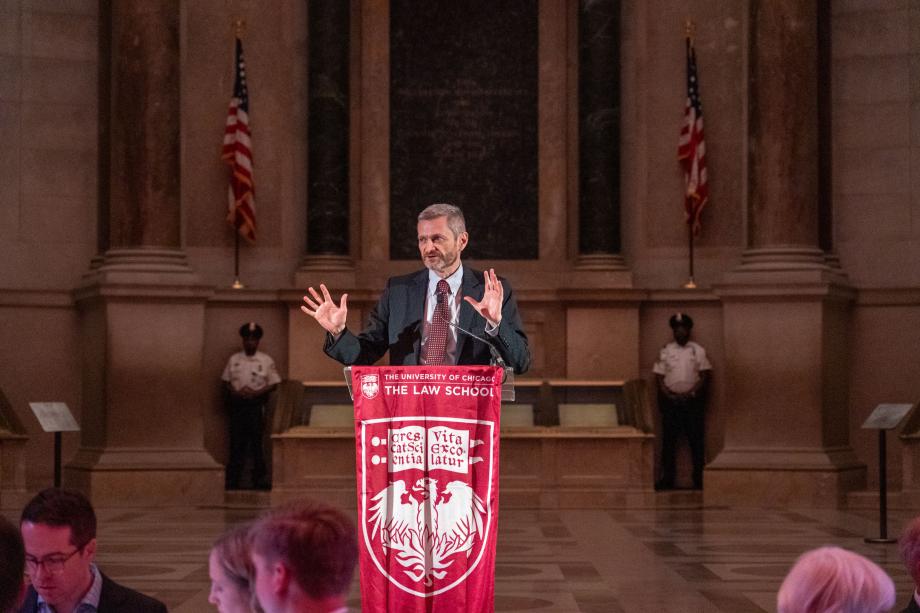 In his introductory remarks, Dean Thomas J. Miles reflected on the origins and impact of the Rubenstein Scholars program and thanked David M. Rubenstein for his incredible generosity to the Law School. Dean Thomas Miles standing at a podium draped with the UChicago logo and shield inside the National Archives Museum event space. Miles faces the audience of attendees while speaking and gesturing his hands forward.