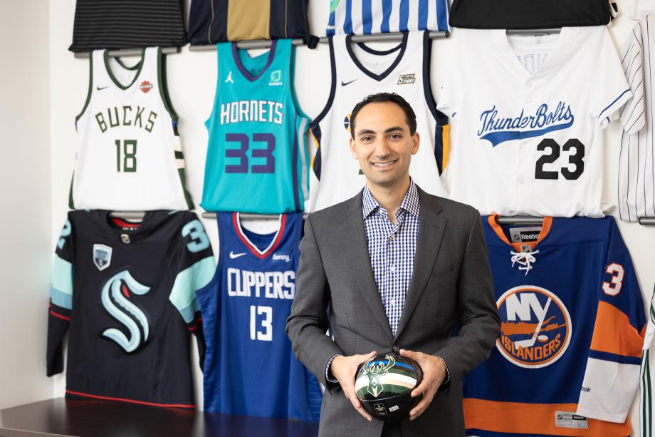 Daniel Render holds a ball with jerseys from the Hornets, ThunderBolts, Clippers, and NY Islanders, and Bucks behind him.