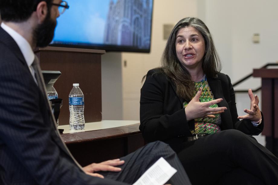 A woman gesturing while she speaks to a man seated next to her in a classroom.