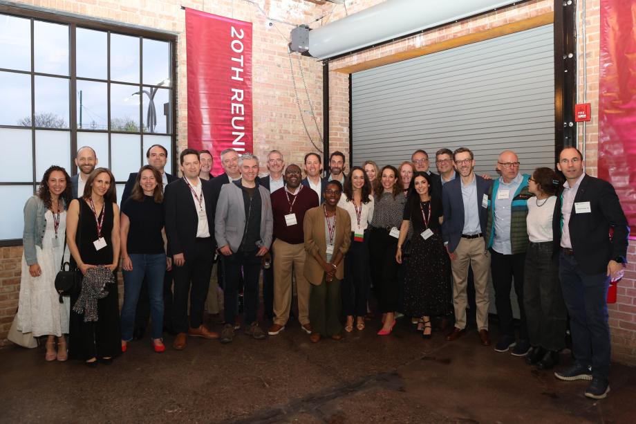 A large group of people gathered together to pose for a photo. Behind them is a brick wall and a large banner that says 20th Reunion.