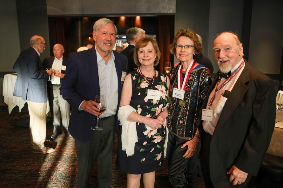 Four people who are poshly dressed are standing side by side posing for a photo.
