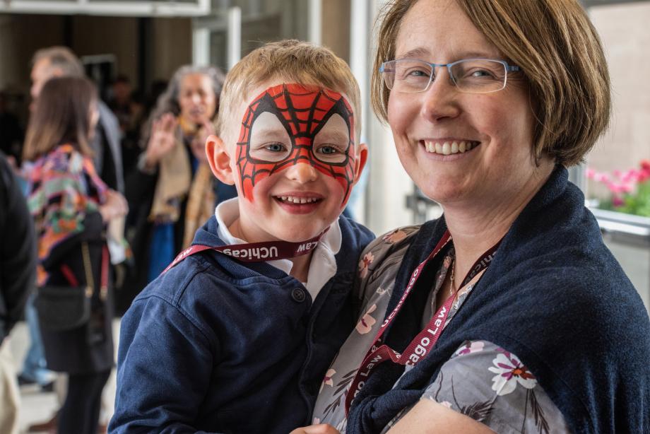 A close-up of a woman smiling while holding a small child whose face is painted red to resemble Spiderman.