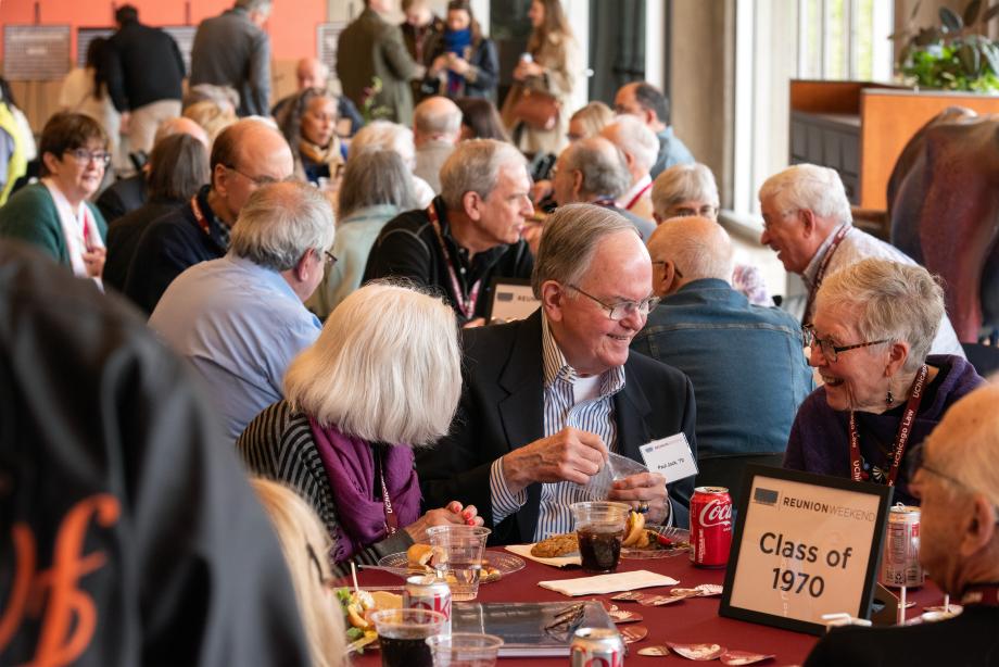 A room filled with people sitting at round tables eating and conversing with one another.