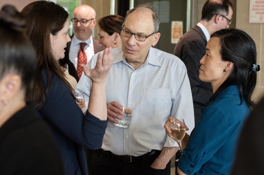 Three people are standing close together talking while holding beverages