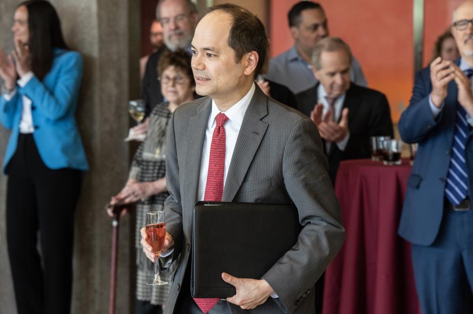 William Hubbard wearing a grey suit and red tie walks to the lectern to give a speech