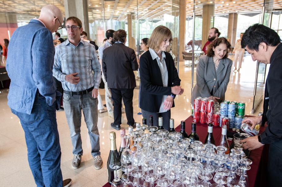 Two women are seen standing over a bartending table being served a drink