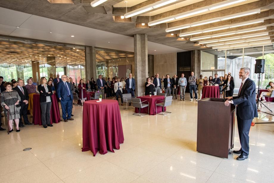 A wide-shot view of Thomas Miles at the lectern addressing people standing at tall round tables listening to him speak