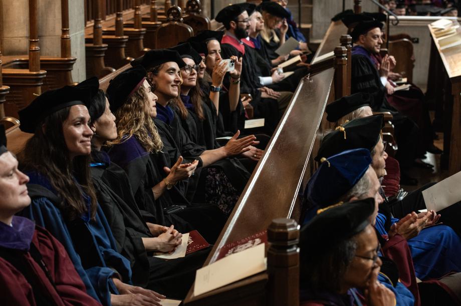 Members of the faculty proudly look on at the graduating class. A side view of people sitting in pews wearing graduation garb looking on at the ceremony.