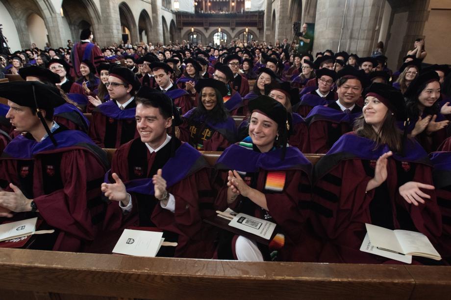 Graduates celebrate each other with enthusiastic applause. A row of graduating students sitting in pews smiling in clapping.