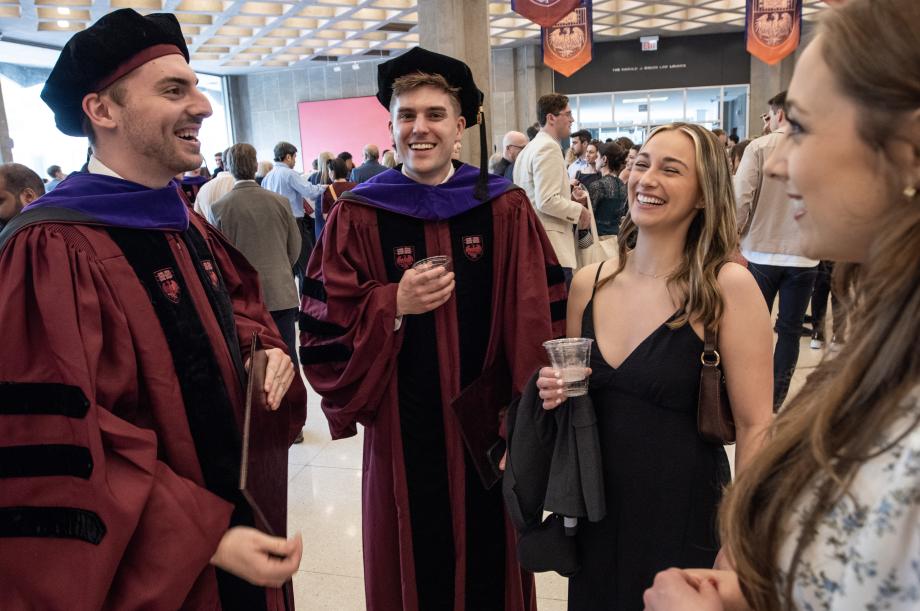 There was no shortage of smiles on the momentous day. Two men wearing graduation garb stand in a semi circle with two women wearing ordinary but dressy clothes; they are all laughing and talking.