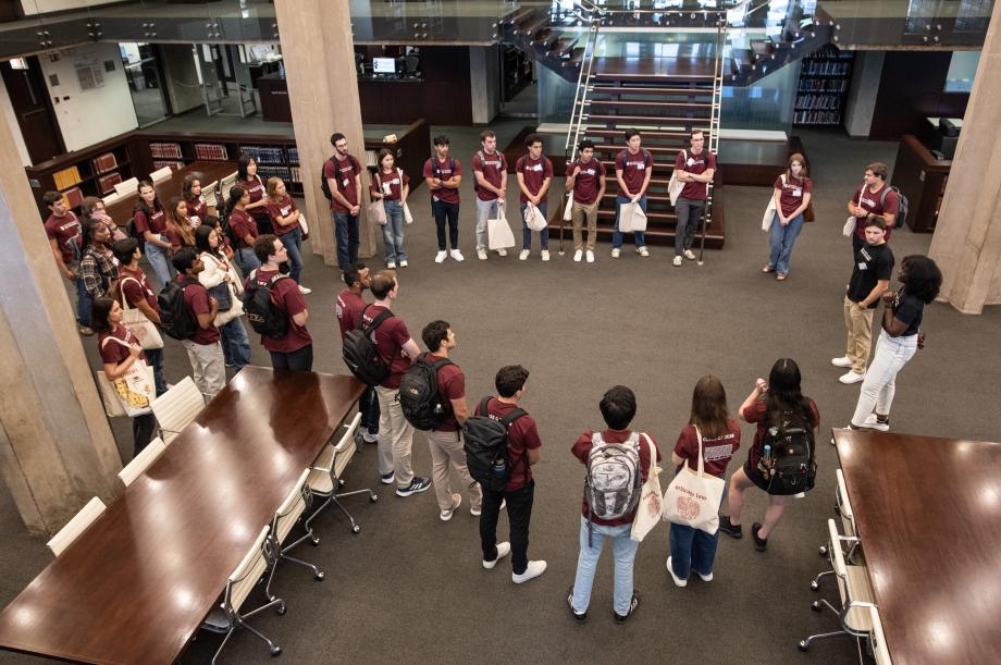 A group of students standing in a library being given a tour.