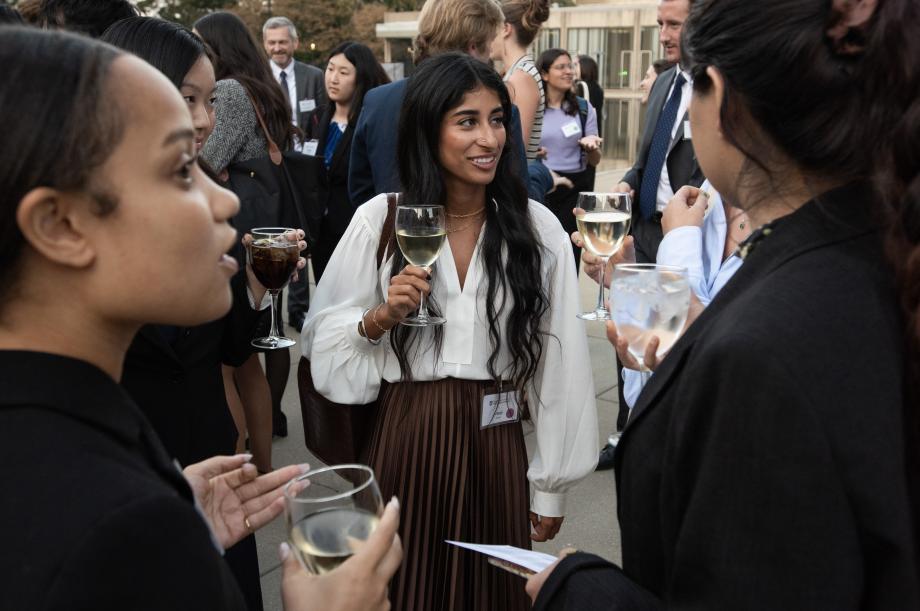 Students standing outside dressed in formal attire and holding glasses of wine.