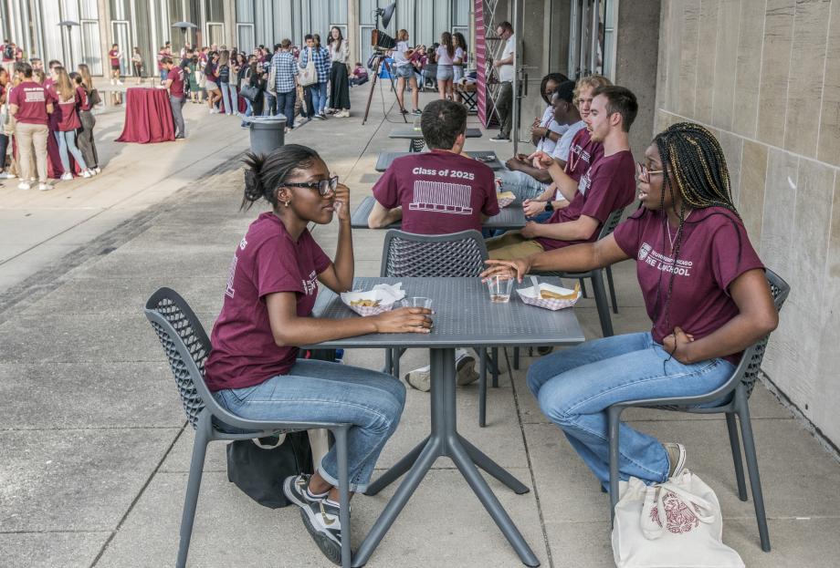 Students sit at tables outside in front of the Law School, beside the Reflecting Pool.