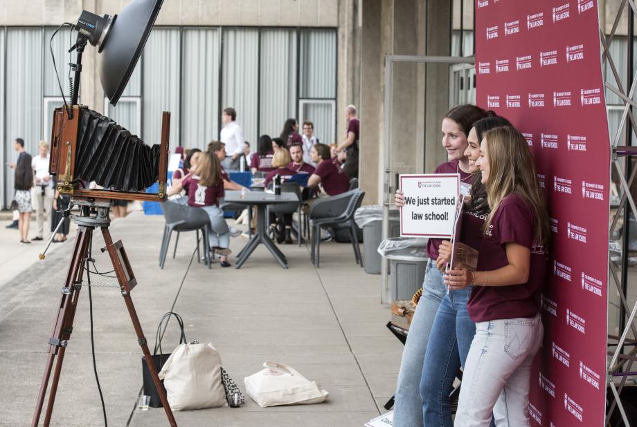 Two students pose in front of a a camera holding a sign that says, "We just started law school!"