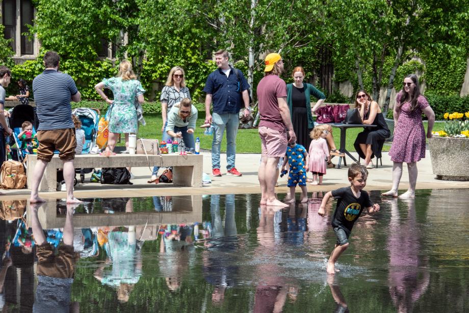 Alumni and their children enjoy a splash in the Law School reflecting pool on "family fun" day. Children and parents wading in a shallow pool on a sunny day.
