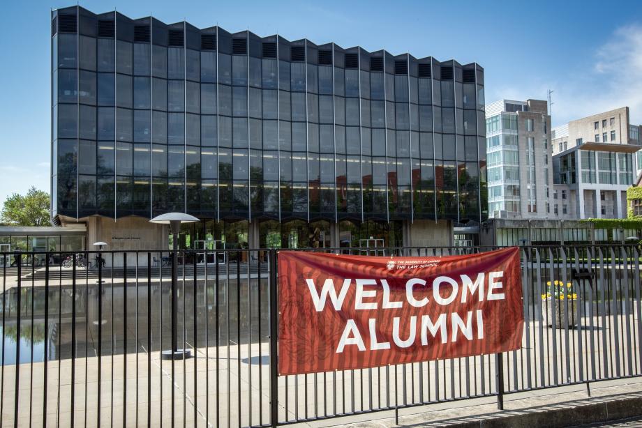A perfect spring day welcomed alumni back to the Laird Bell Law Quadrangle. A large rectangular glass building stands tall against a bright blue sky. A banner hangs on a gate in front of it that says Welcome Alumni.