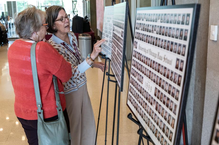 Alumni find familiar faces in the photo boards displayed in the Green Louge. Two woman looking at a poster board of people's faces.