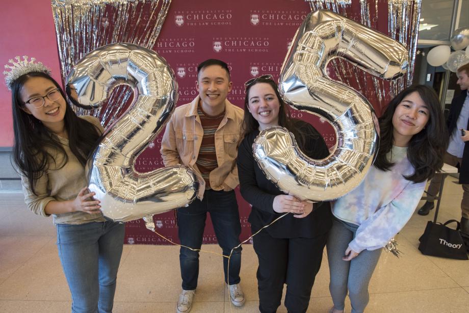 Students posing with large silver balloons shaped as a 2 and a 5.