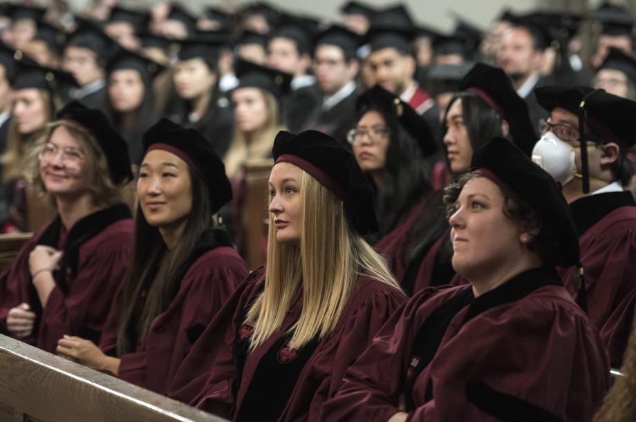 Students in the caps and gowns, sitting in the pews inside the chapel.