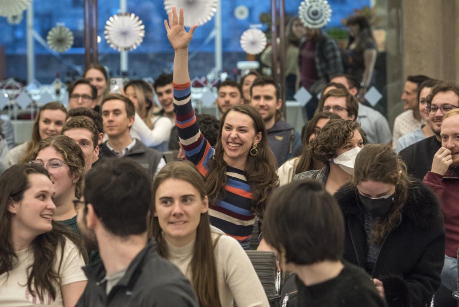 A smiling student who is seated in a group in the Green Lounge raises her hand to bid on an item during the live auction.