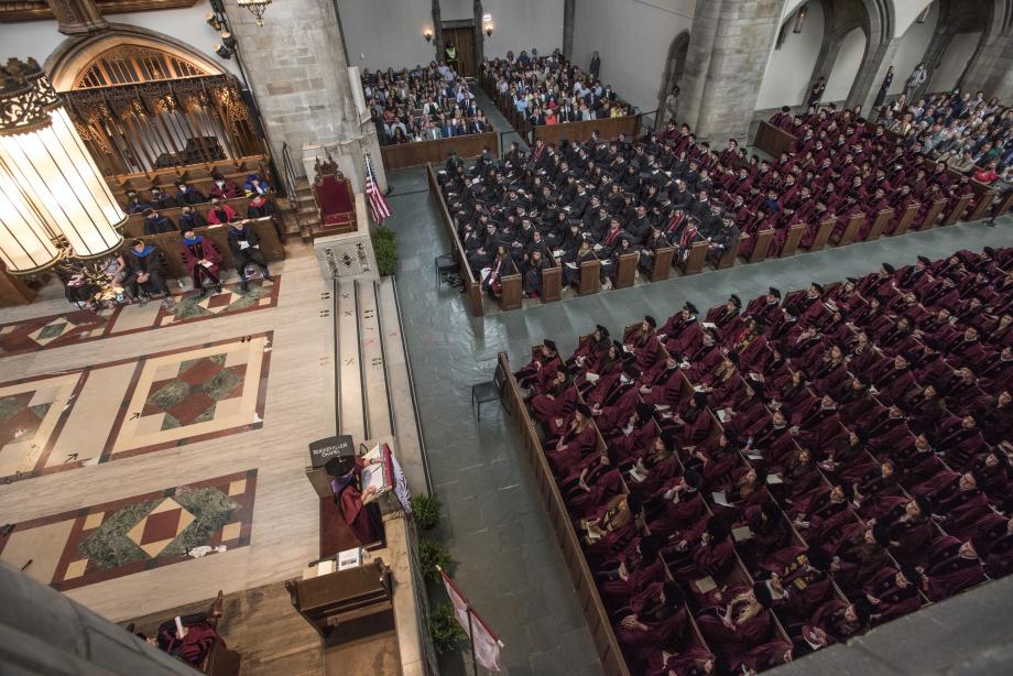 View from balcony in Rockefeller Chapel showing a speaker at the podium and the graduates seated in pews. 