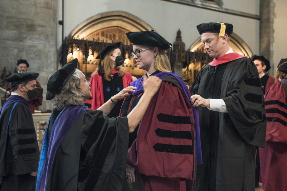 Two faculty hooders place a hood on a new JD graduate.