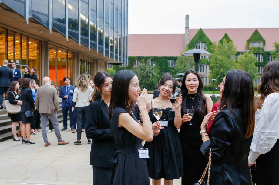 Students stand in cocktail attire with drinks in hand as they chat together.