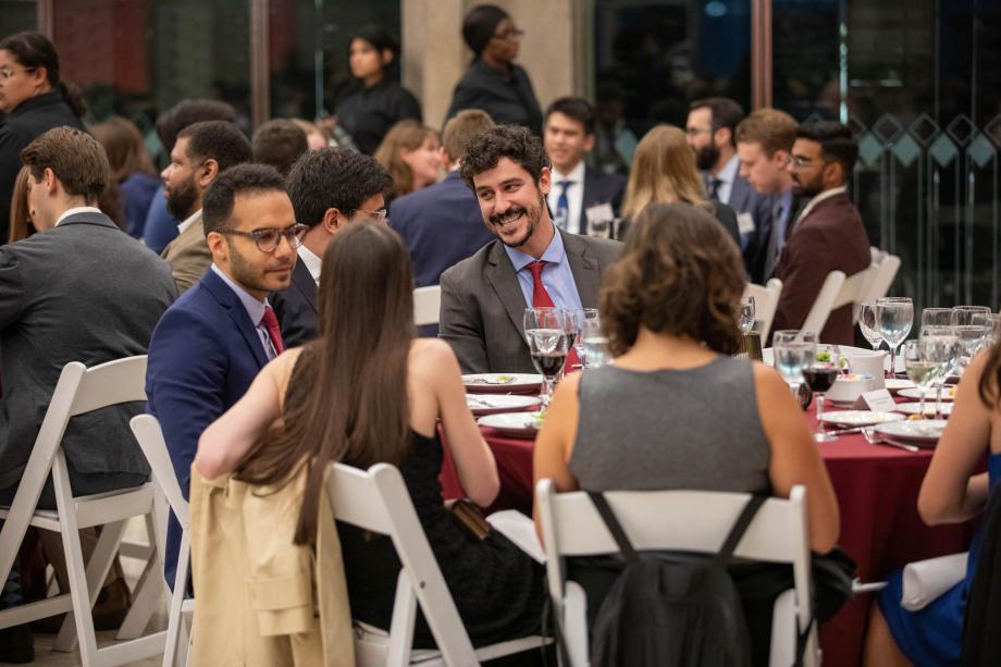 Students in cocktail attire sit at round tables for dinner.