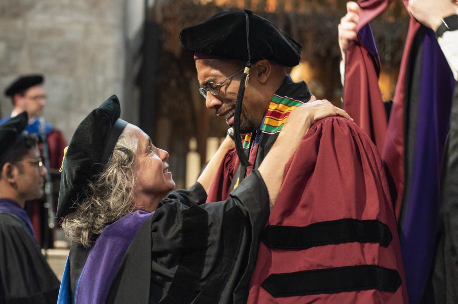 Buss shares a moment with Andre Washington, ’19, as Masur prepares to present his hood. Buss shares a moment with Andre Washington, ’19, as Masur prepares to present his hood.