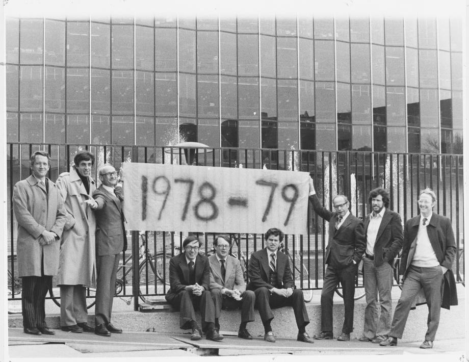 Geoffrey Stone (second from right) with fellow Law School faculty. Nine men in suit jackets stand in front of the Law School building, holding a banner that says, "1978-79"