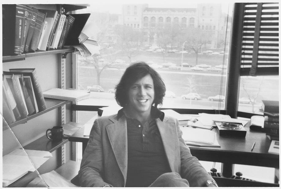 Geoffrey Stone in his early years at the Law School, circa 1973. Stone, in a polo and jacket, sits at his desk with campus views behind him.