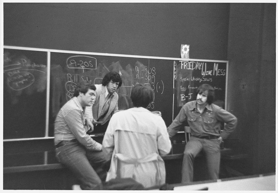 Four people huddle in front of a blackboard in a classroom.