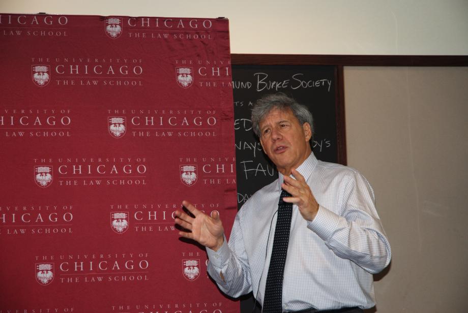 Geoffrey Stone delivering a “NASA talk” in 2013. Stone, in a shirt and tie, motions with his hands in front of a step and repeat with the Law School logo.