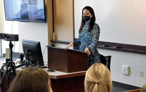 A speaker stands at a lectern with her mask on as students listen.