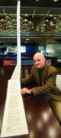 Omri Ben-Shahar sits next to a printed disclosure, pages taped end to end, stretching from the ceiling on the 3rd floor to a table on the 2nd floor.