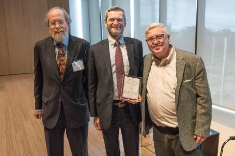 Frank Easterbrook, Dean Miles, holding an award, and Daniel Fischel, pose for the camera