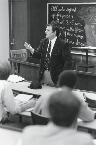 Hutchinson lecturing students in front of a black board with his right hand out