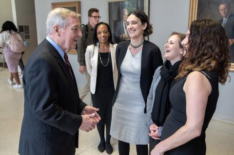 Senator Durbin stands in a hallway with Professors Miller, Zunkel, and Siegler, who are all laughing.