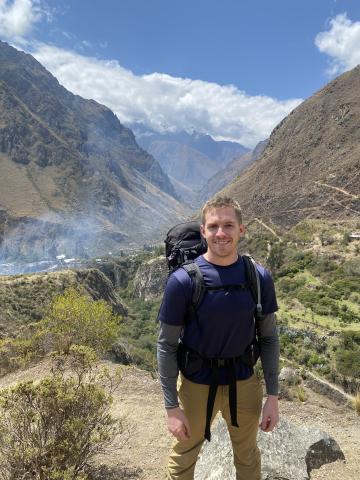 Alec Hubbard with a backpack in front of a mountain scene.