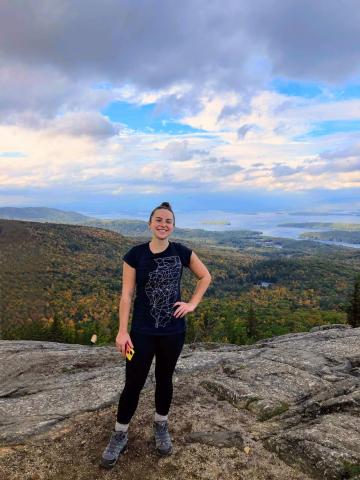 Marina Rioux on a rocky outcrop overlooking dense woods and water on the horizon