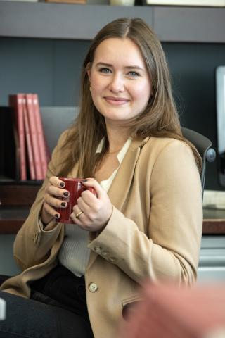 Woman sitting in an office chair holding a coffee mug and smiling at the camera