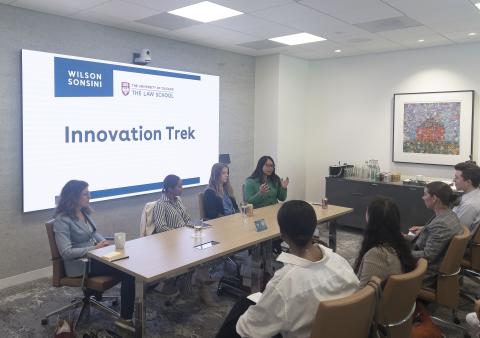 Four women sitting at a table talking to students in a conference room.